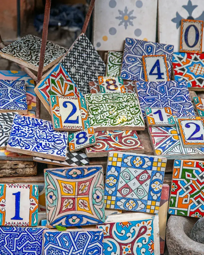 Conjunto de azulejos pintados a mano con motivos geométricos y florales apilados sobre una superficie de madera